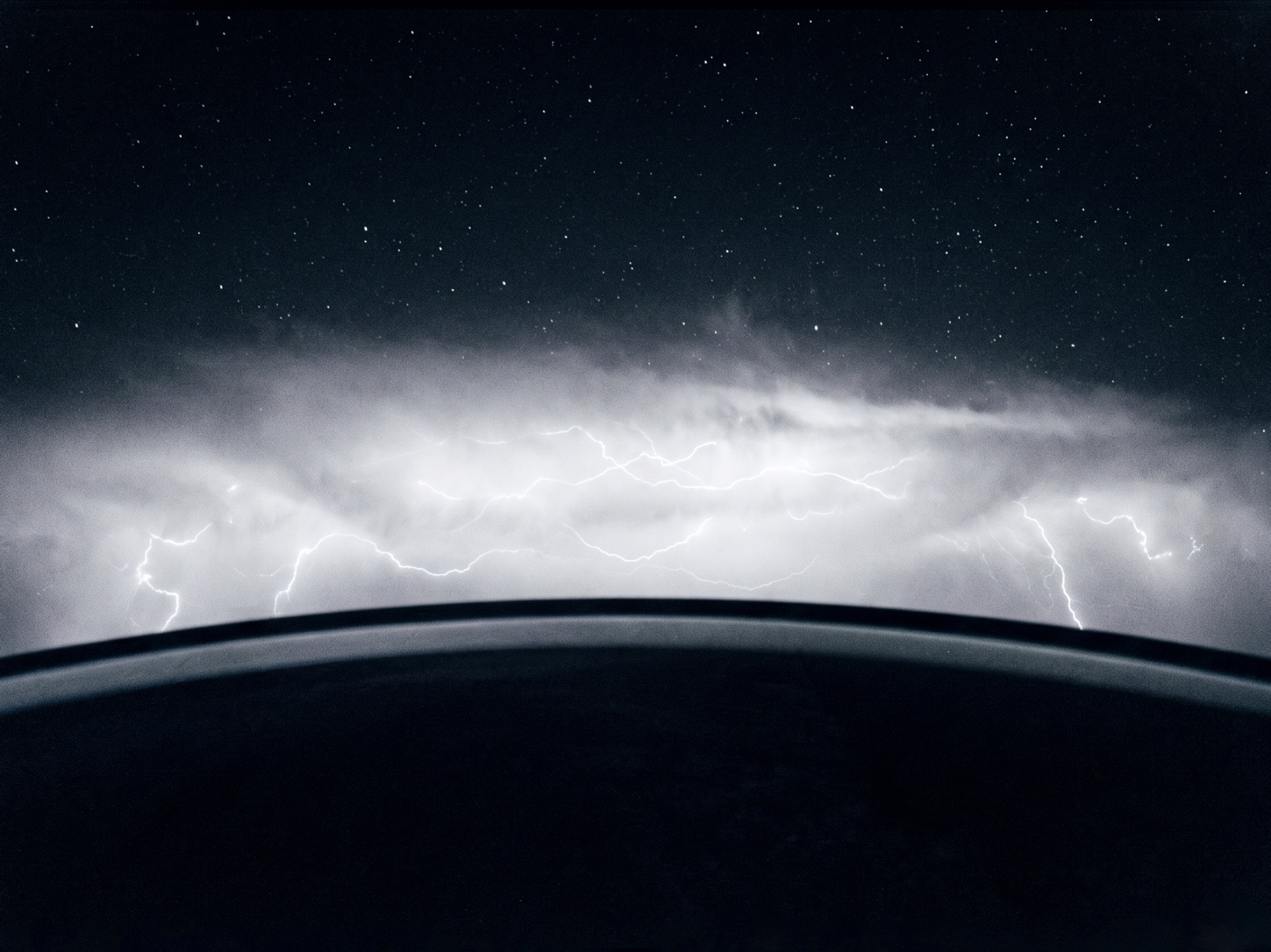 Lightning and clouds seen beyond a dark curved horizon